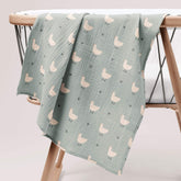 Minty duck muslin swaddle draped over wooden baby stand
